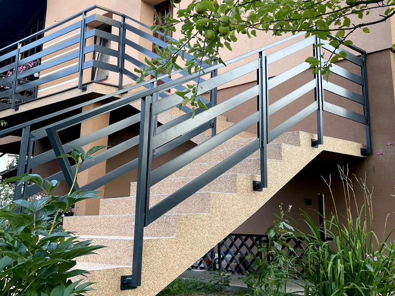 Zewnętrzne schody z metalową balustradą i nowoczesnym wykończeniem przy budynku mieszkalnym.