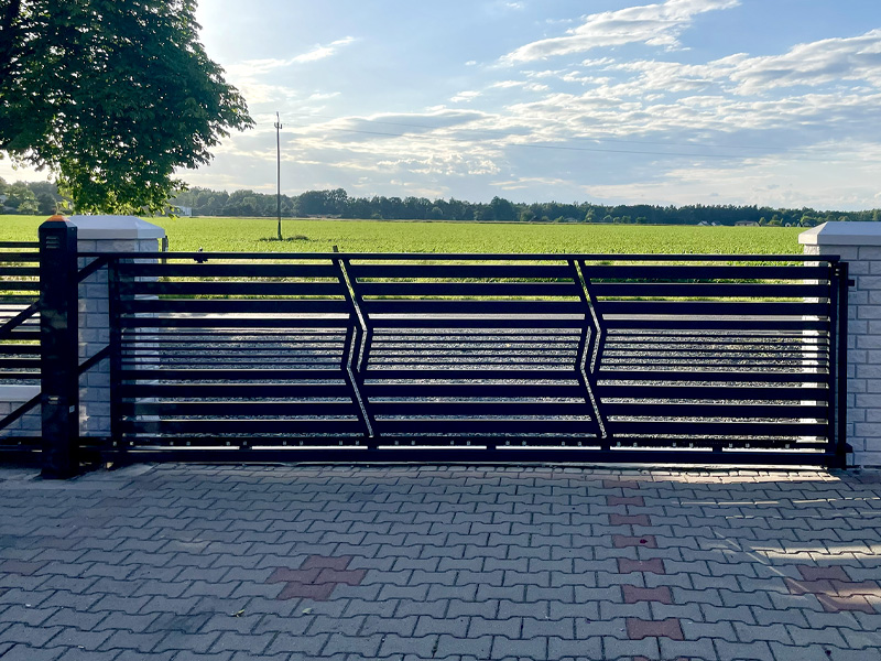 Automatyczna brama przesuwna ze stali z poziomymi profilami przy ogrodzeniu posesji.